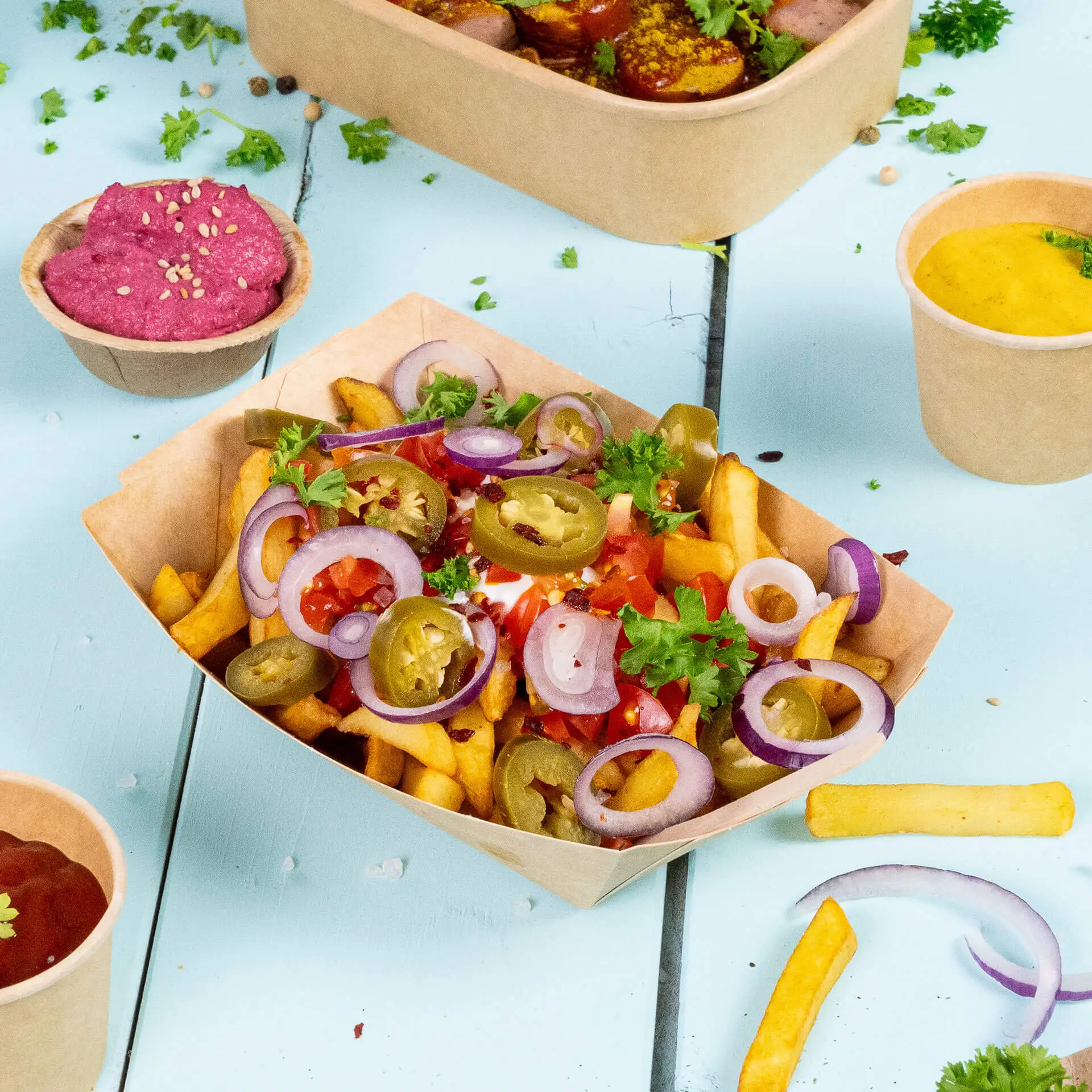 Brown cardboard snack tray filled with french fries, tomatoes, jalapeños, and onions; served with sauces in cups.